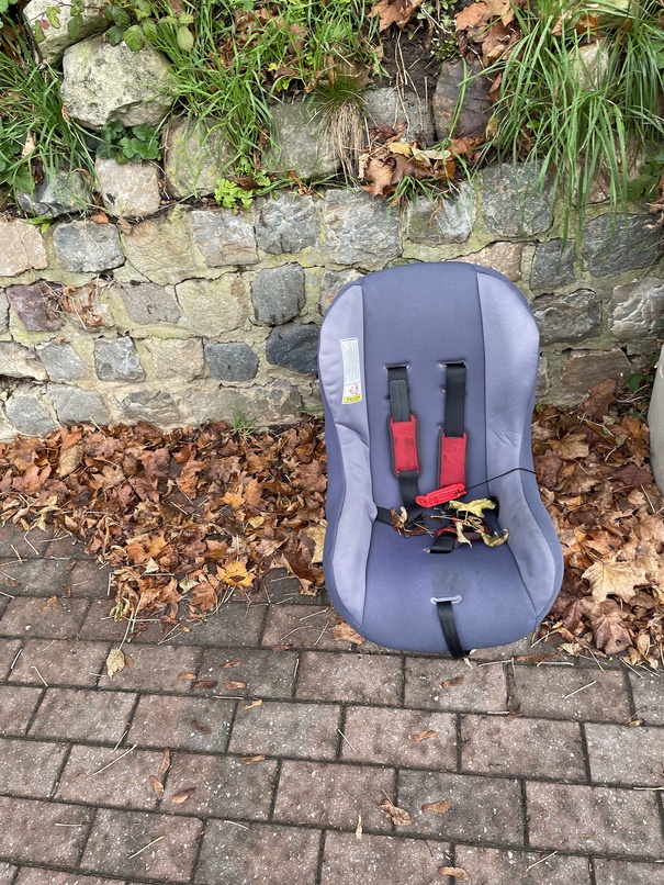 the image shows a baby chair thrown out on a sidewalk, with autumn leaves"